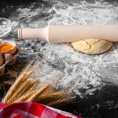 Pizza pişirmek için gerekli malzemeler siyah bir masada yatıyor. Hamur, yumurta, kulak