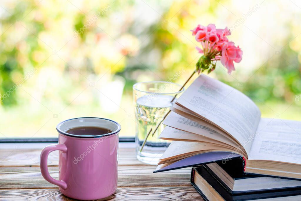 A pink cup of tea stands on a wooden window sill against the backdrop of a garden