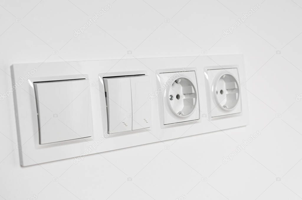 White plastic walk-through switches and sockets on a white wall. Repairs