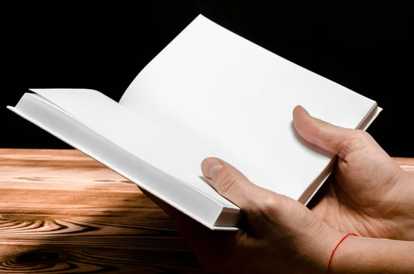 Чоловічі руки тримають білу книгу на дерев'яному тлі — стокове фото