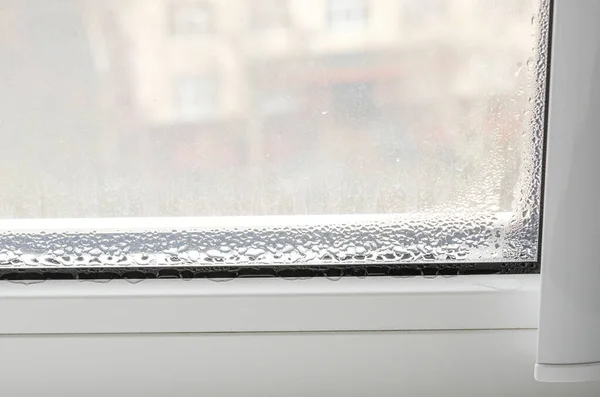 Beyaz metal-plastik bir pencerede yoğunlaşan damlalar. Ekoloji