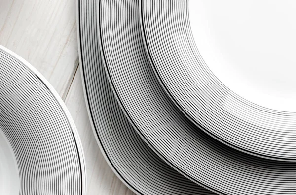 Beyaz yuvarlak, klasik, gri desenli porselen plakalar beyaz ahşap bir masa üzerinde duruyor.