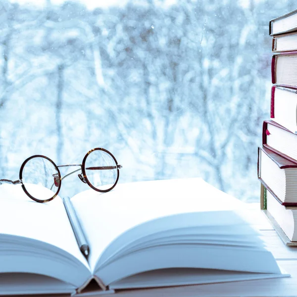 Round vintage reading glasses lie on a white book layout against the backdrop of the winter forest
