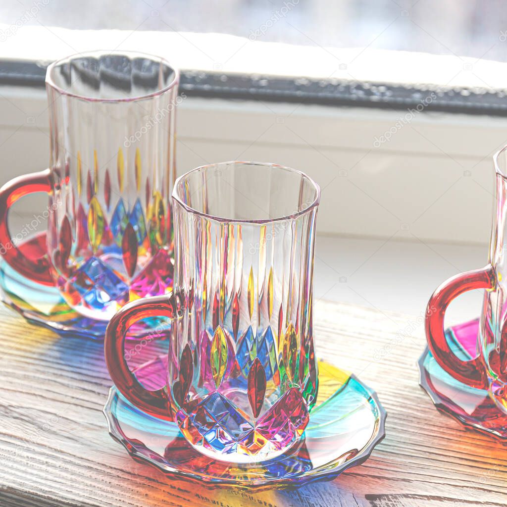 Multi-colored glass cups and saucers for coffee and tea stand on a wooden tray