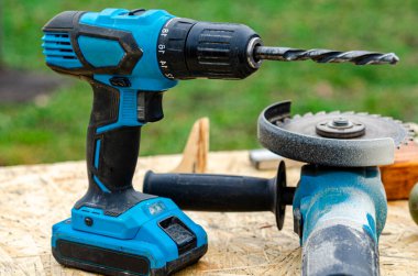 Bahçedeki ahşap bir masada mavi bir batarya matkabı duruyor. Elektro talimatlar. Tamir et. İnşaat