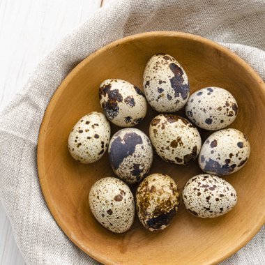 Bıldırcın yumurtaları beyaz ahşap bir masada, tahta bir tabakta yatar.
