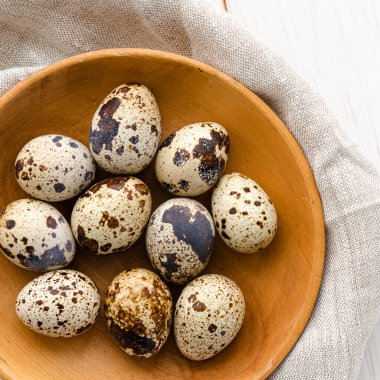 Bıldırcın yumurtaları beyaz ahşap bir masada, tahta bir tabakta yatar.