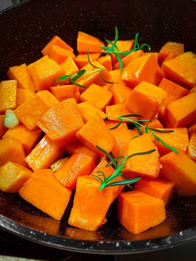 Siyah tavada yeşil biberiye dalları olan turuncu parlak balkabağı parçaları.