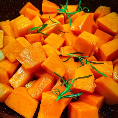 Siyah tavada yeşil biberiye dalları olan turuncu parlak balkabağı parçaları.