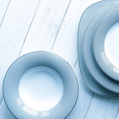 Beyaz yuvarlak, klasik, gri desenli porselen plakalar beyaz ahşap bir masa üzerinde duruyor.