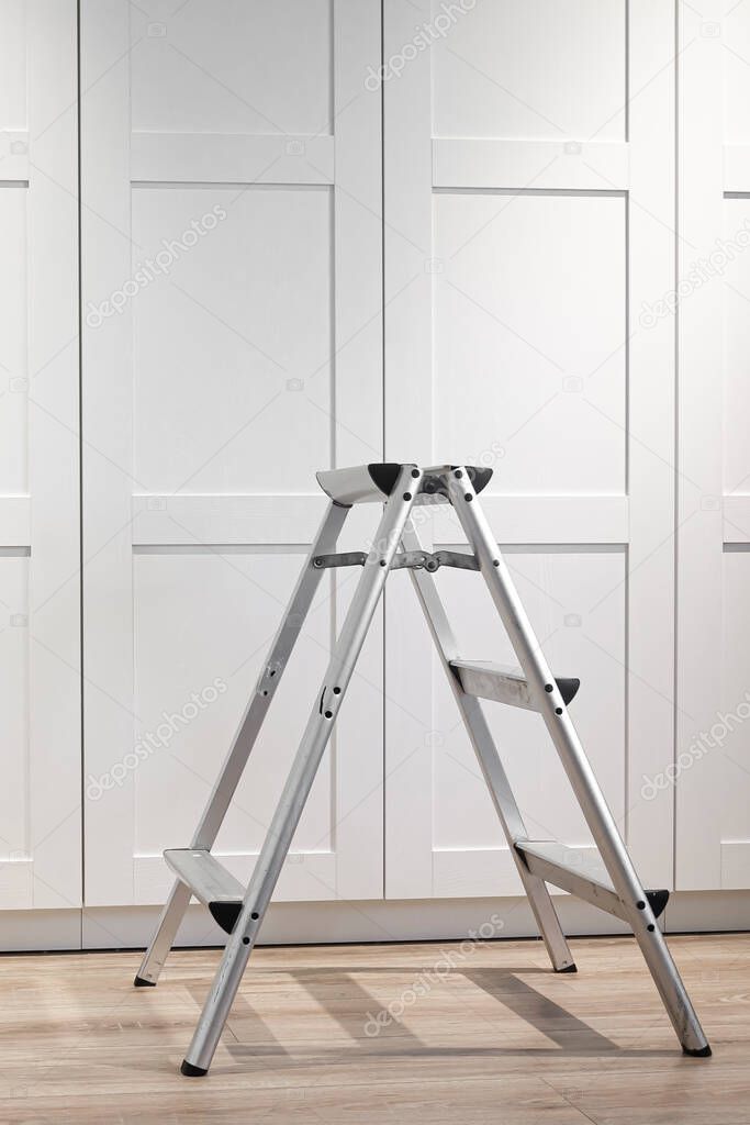 The folding stepladder for repair and installation of furniture stands on a wood floor. Repair