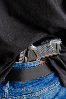 Kot kemerinin altına saklanmış bir tabanca. Bir kişi kot kemerinin altında tabanca saklıyor..