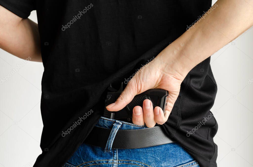 a man in jeans and a t-shirt holds a gun in his hand from the back