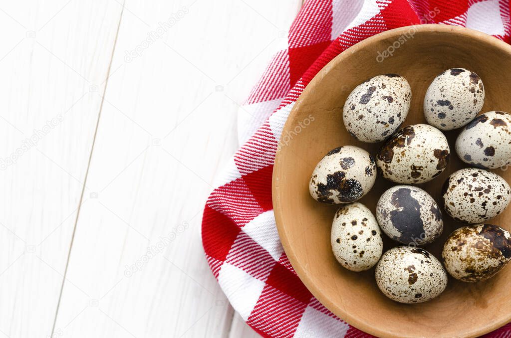The quail eggs lie on a wooden plate on a white wooden table