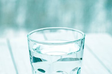 Saf erimiş suyla dolu bir bardak beyaz bir masanın üzerinde duruyor.