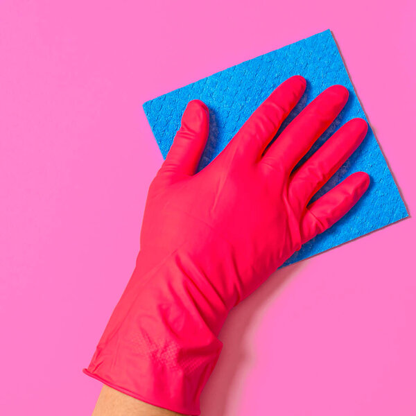 Blue house cleaning sponge in hand in red rubber glove on pink background