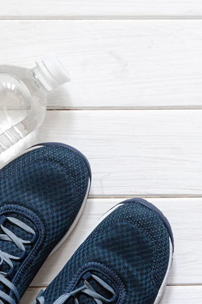 Beyaz ahşap arka planda spor, üst manzara, kopyalama alanı. Mavi spor ayakkabılar, mavi halterler ve beyaz pullar.