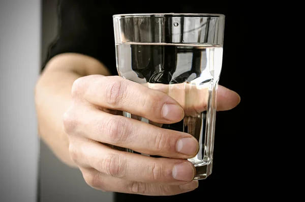 Hand mit einem Glas reinem Quellwasser auf schwarzem Hintergrund — Stockfoto