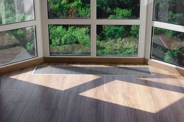 Panoramik pencereleri ısıtmak için yere konmuş koruyucu radyatör ızgarası. Yerdeki ahşap zeminde havalandırmalı ısıtma ızgarası.