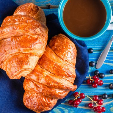 Avrupa otelinde kahvaltı: Sütlü ve kruvasanlı kahve, reçel ve ahududu ve ahşap bir masada böğürtlen. Kupa yazıtlarında Fransızca