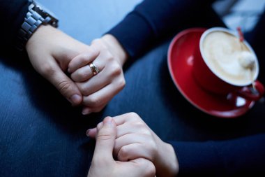 Kahve dükkanında birbirine sarılan erkek ve kadın ellerinin yakın plan fotoğrafı. Kafede romantik bir çift. Sevgililer günün kutlu olsun. Kış tatili kutlaması.