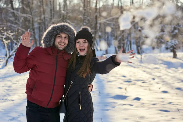 Young couple in love, enjoying winter sunny weather outside in snowy park forest. Brunette man in red jacket and woman in black throwing snow. Christmas and new year holidays joy. Romantic date.