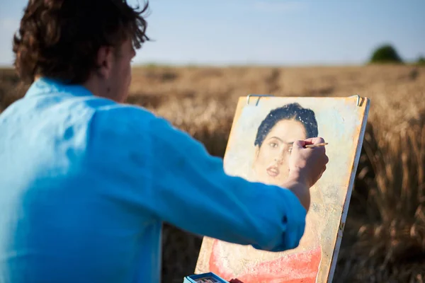 Young male artist, drawing portrait on canvas painting on wheat field in summer. Painting workshop in rural countryside. Artistic education modern concept. Outdoors leisure activities.