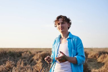 Kirli, boyalı elli, fırça tutan, açık mavi gökyüzüyle buğday tarlasında duran bir erkek sanatçı. Sanatsal eğitim aktivitesi. Açık havada resim atölyesi. Yaz eğlencesi.