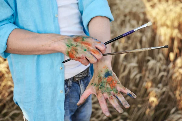 Close Picture Dirty Paint Hands Holding Brushes Front Yellow Wheat — Stock Photo, Image