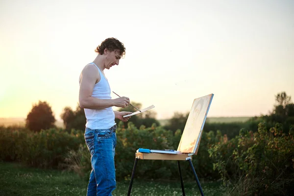 Młody Artysta Stojący Przy Sztaludze Malujący Latem Płótnie Zielonym Polu — Zdjęcie stockowe