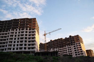 Mavi güneşli gökyüzünün önünde kocaman çok katlı apartmanlar ve vinç olan inşaat alanı. Şehrin banliyölerinde inşaat işlemi. Kalacak yer geliştirme.