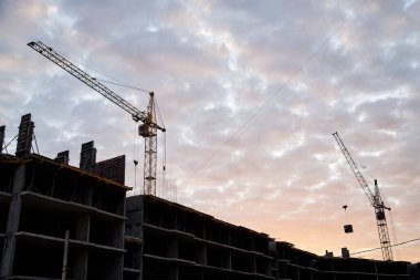 Mavi güneşli gökyüzünün önünde kocaman çok katlı apartmanlar ve vinç olan inşaat alanı. Şehrin banliyölerinde inşaat işlemi. Kalacak yer geliştirme.