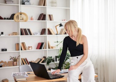 Genç sarışın kadın, siyah beyaz pantolon giyiyor, masada oturuyor, dizüstü bilgisayarla çalışıyor. Ofis müdürü iş yerinde, sunum için hazırlanıyor. Şirkette hafif bir ofiste çalışan bir kadın..