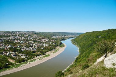 Nehirle çevrili küçük bir kasabanın manzarası. Mavi güneşli gökyüzü ve parlak yeşil bitkilerle güzel bir doğa manzarası. Yaz tatili ıssız yerlere.