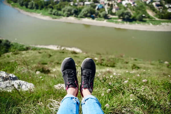 Close-up picture of female legs lifted over small town, surrounded by river.Beautiful natural countryside landscape with blue sunny sky,bright green plants.Summer getaway vacation into isolated places