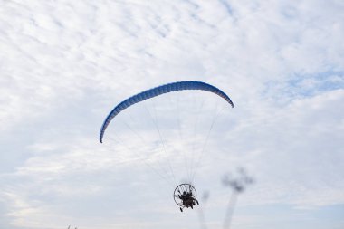 Sonbahar sabahı bulutlu gökyüzünde mavi paraşütlü bir paraşüt. Kırsal kesimde paraşütle atlama aktivitesi. Hafta sonu boş zaman ve hobi. Paramotor makinesinde ekstrem spor uçuşu.