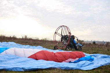 Mavi paraşütlü paraşüt bulutlu gökyüzünde uçmaya hazır. Kırsal kesimde paraşütle atlama aktivitesi. Hafta sonu boş zaman ve hobi. Paramotor makinesinde ekstrem spor uçuşu.