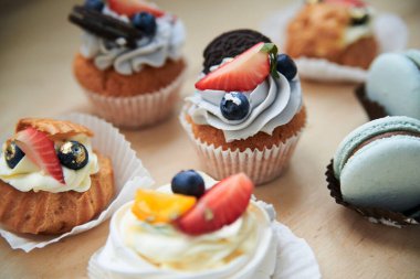 Krem peynirli, meyveli ve naneli kurabiyelerin yakın plan fotoğrafı. Ahşap masa büfesinde renkli tatlı hamur işleri. Bayram kutlaması. Parti. Süslü mini tatlılar.