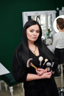 İş yerindeki makyaj sanatçısının portresi. Elinde çeşitli fırçalar ve paletler var. Güzellik salonunda çalışma süreci. Profesyonel stilistin yardımıyla gala yemeğine hazırlanıyorum..