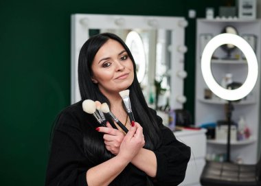 İş yerindeki makyaj sanatçısının portresi. Elinde çeşitli fırçalar ve paletler var. Güzellik salonunda çalışma süreci. Profesyonel stilistin yardımıyla gala yemeğine hazırlanıyorum..