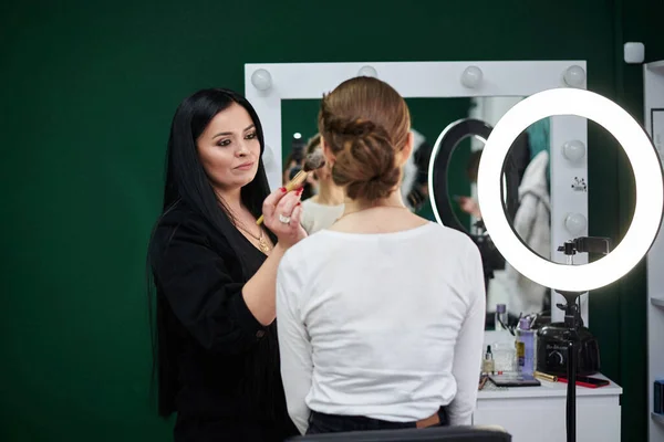 花嫁は結婚式の準備をする 大きなメイクブラシで女性のクライアントの顔に赤面を適用するプロのメイクアップアーティスト 美容室での作業プロセス メイクアップモデルのクローズアップ写真 — ストック写真