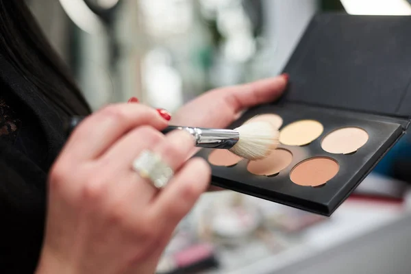 Close-up picture of make-up tools in female hands in beauty salon. Professional eye shadow palette in brown shades for work of make-up artist. Work process in beauty studio.