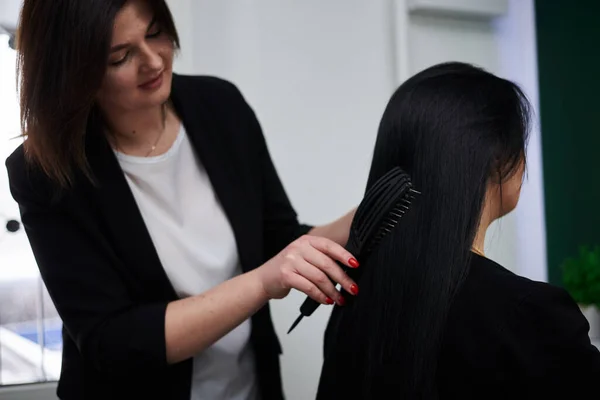 女性のクライアントのためのヘアスタイルを作るプロの美容師 彼女の黒い光沢のある髪をブラッシング 理容室での作業工程のクローズアップ写真 若いですブルネット女性取得準備のためにパーティー — ストック写真