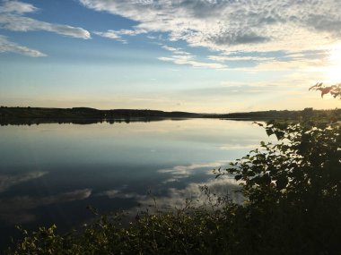 Akşamları gölün üzerinde güzel bir günbatımı. Kırsal kesimde sakin bir manzara. Doğada derin meditasyon. Fotoğraf için sihirli bir loş ışık saati. Gölün panoramik manzarası.