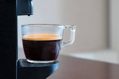 Kapsül makinesinin ferahlatıcı espresso 'sunu evdeki bir bardağa boşalt. Kahve molası kavramı.