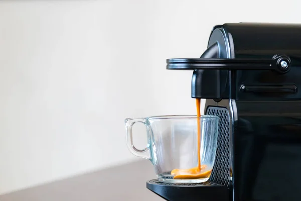 Kapsül makinesinin ferahlatıcı espresso 'sunu evdeki bir bardağa boşalt. Kahve molası kavramı.