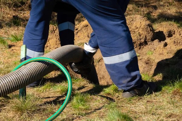 Boru tutan işçi, dışarıdaki kanalizasyon temizleme servisini sağlıyor. Kanalizasyon pompalama makinesi tıkanmış rögar kapağını açıyor
