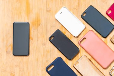 Ahşap arka planda cep telefonları için çok renkli plastik kapaklar ve yanında da bir telefon var.