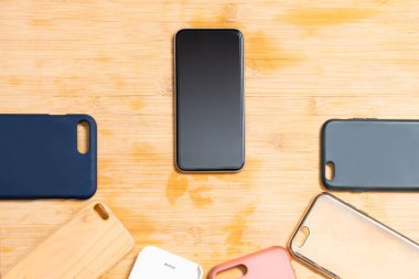 Ahşap arka planda cep telefonları için çok renkli plastik kapaklar ve yanında da bir telefon var.