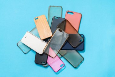 Mavi arka plandaki cep telefonları için çok renkli plastik kapaklar yığını